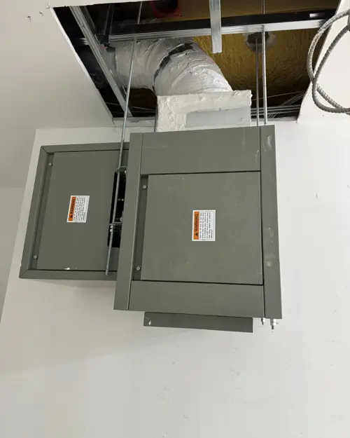 Electrical panels beside an open ceiling with duct